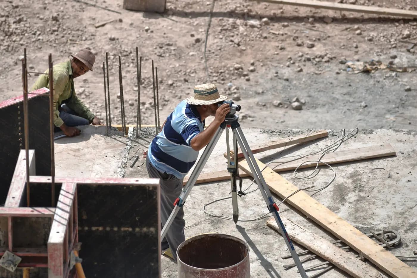 Sur un chantier ensoleillé à Fès, un technicien vise au théodolite pendant qu'un ouvrier prépare les fondations